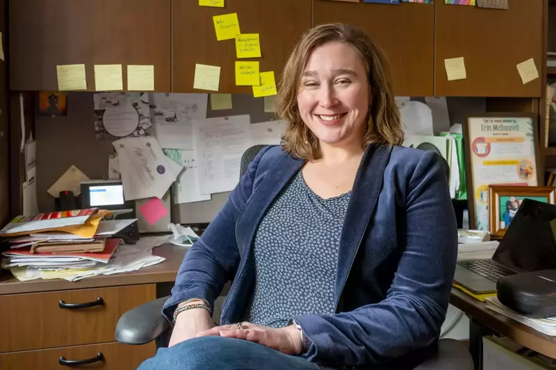 A portrait of Erin McDonnell sitting at a desk with yellow sticky notes on the cabinets
