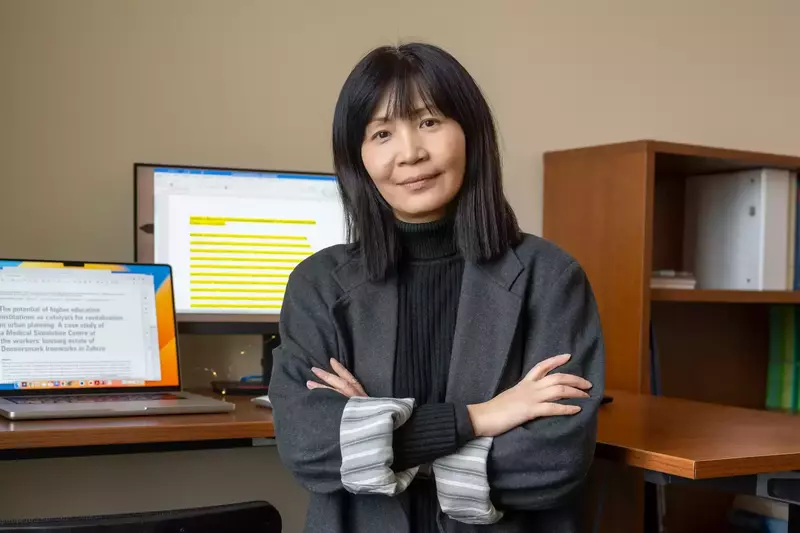 Ming Hu standing in her office with 2 computer screens and bookshelves behind her.