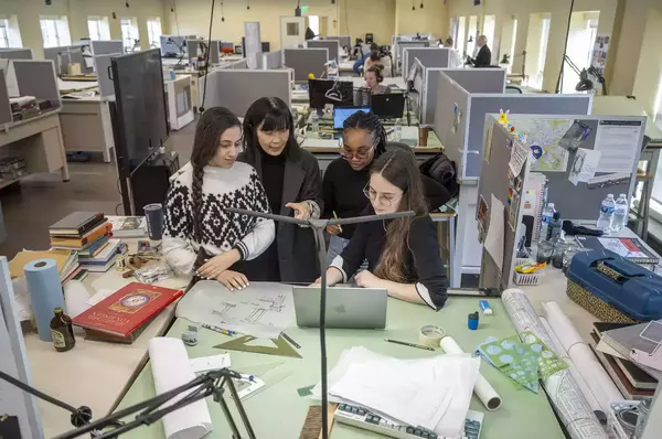 Ming Hu stands at a drafting table with three female architecture students.
