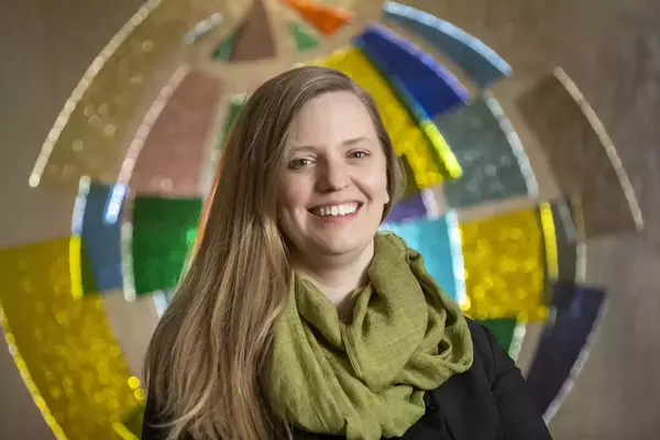Julia Kowalski poses for the camera in front of a stained glass window in the shape of an abstract globe.